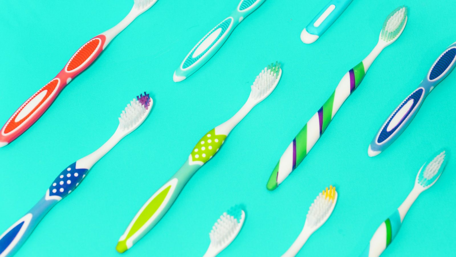 Colorful toothbrushes laid out in a row on a bright teal background